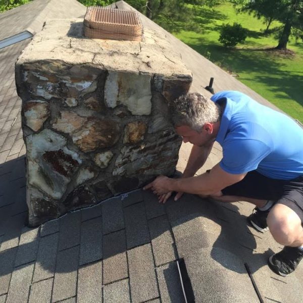 Home inspector examining the flashing around a chimney during a roof inspection in Greensboro, NC. The inspector is checking for leaks and structural issues.