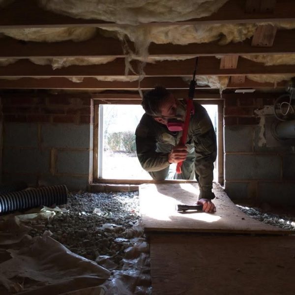 Home inspector examining a crawl space in Greensboro, NC, checking for structural integrity and insulation issues. The inspector is wearing protective gear and using a flashlight to conduct a thorough inspection.