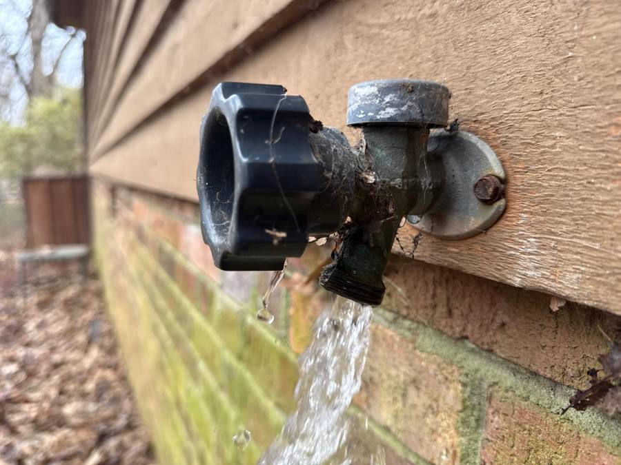 Leaking outdoor faucet with water flowing – home maintenance issue in Greensboro.